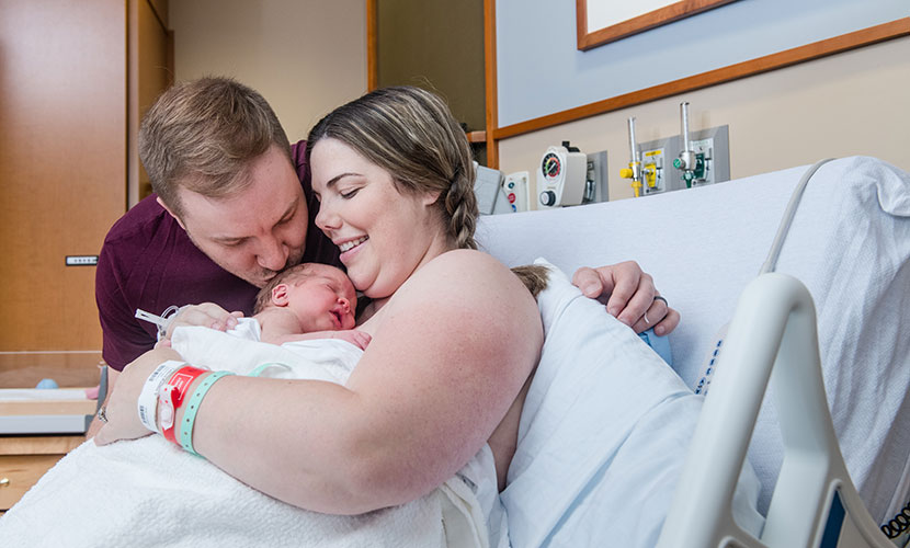 parents with newborn baby, dad kissing baby's head