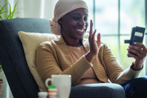 A 55 year old African American woman wearing a headscarf video calls on her smartphone as she sits in her living room.