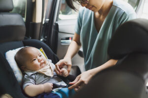 Mother helping her little baby boy son to fasten belt on his car seat in car
